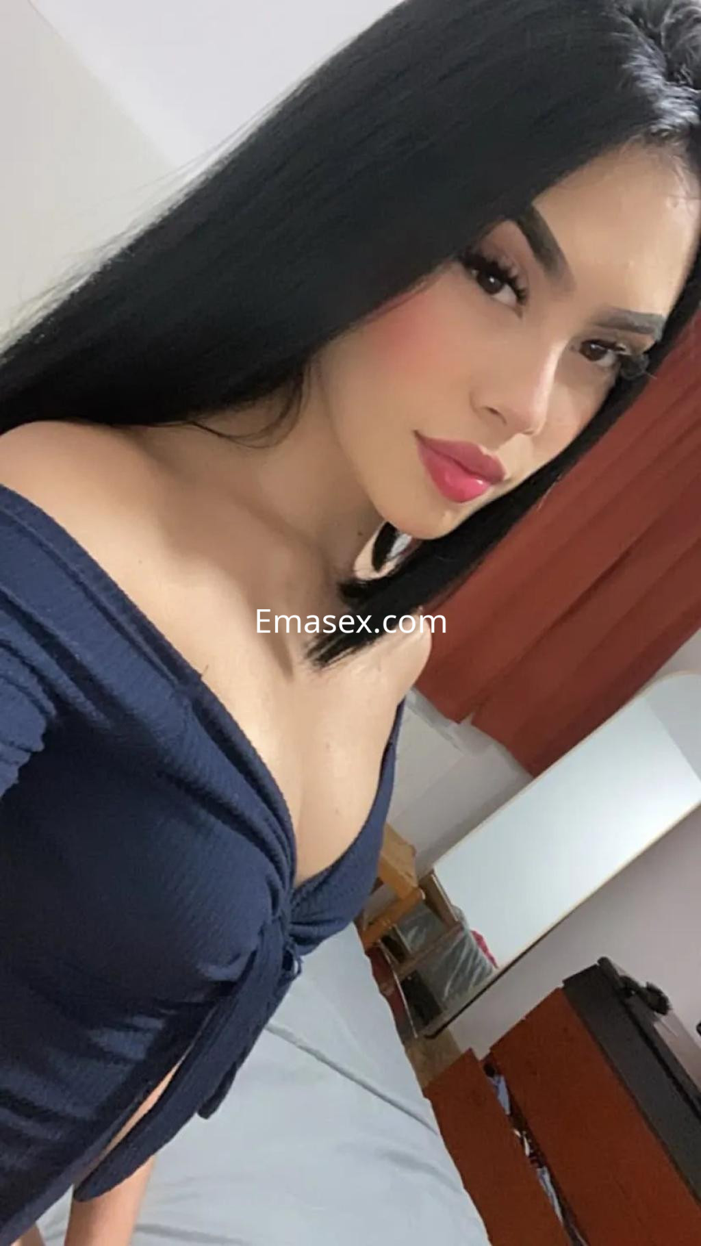 Escort en Gijón con cabello largo y oscuro, vistiendo una blusa azul de hombros descubiertos en un entorno acogedor.