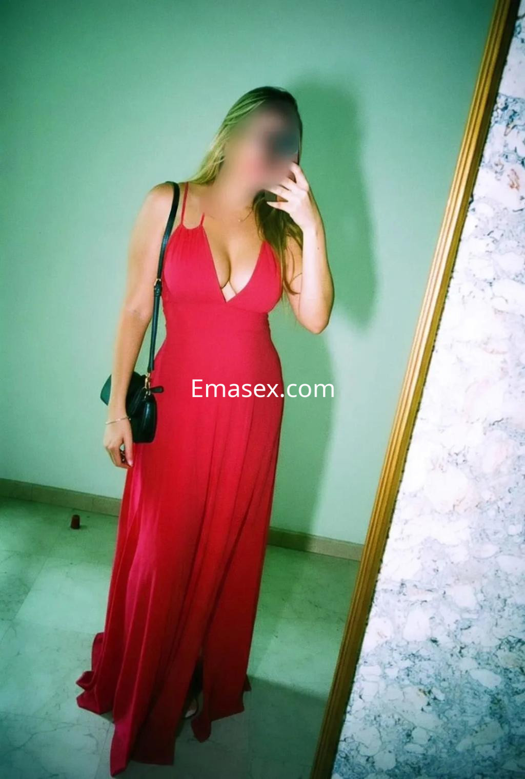 Escort en Valencia viste un elegante vestido rojo con escote profundo, posando frente a un espejo.