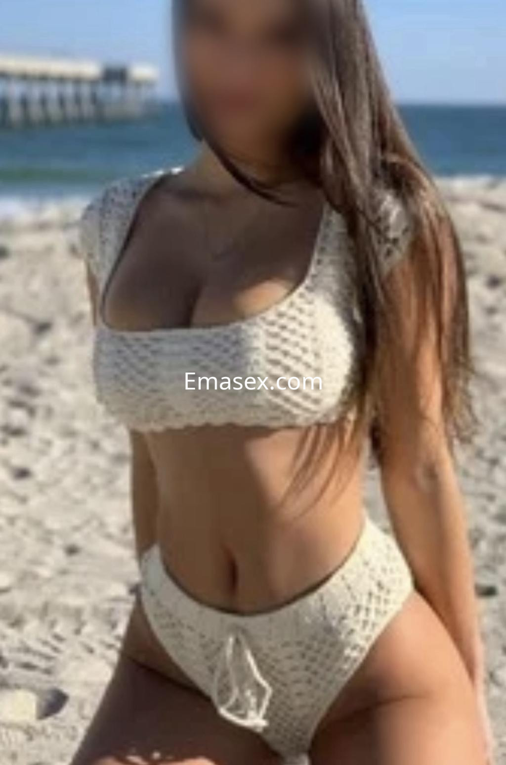 Escort en Donosti con un bikini de crochet claro, sentada en la playa con el mar de fondo.
