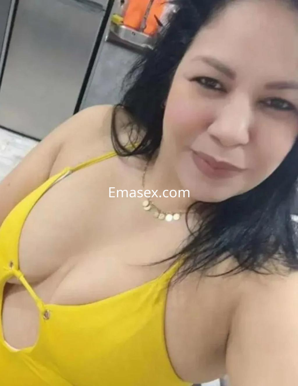 Escort en Córdoba con cabello oscuro, usando un vestido amarillo con escote, sonriendo en un entorno interior.