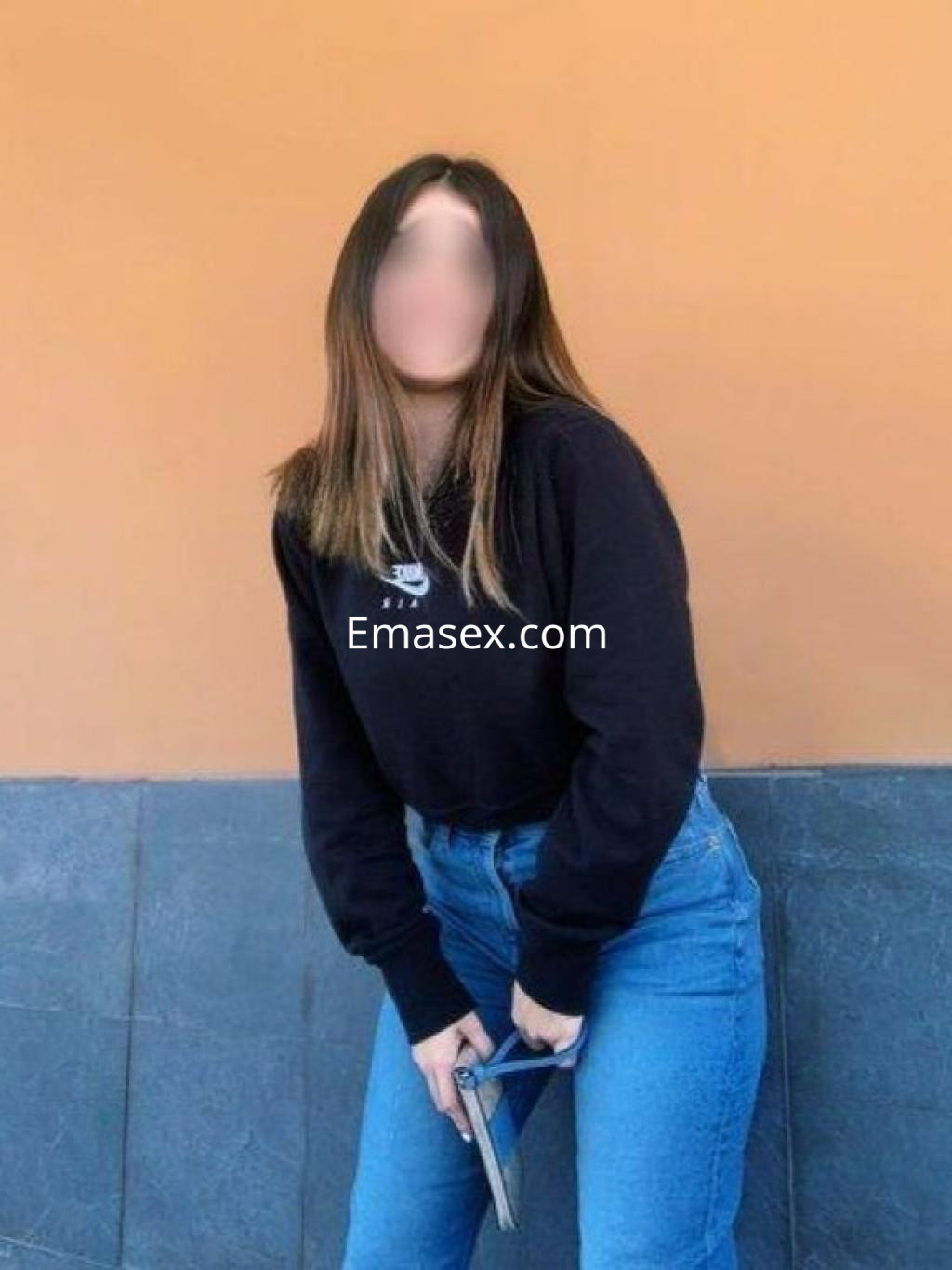 Puta en Zaragoza viste un suéter negro y jeans ajustados, posando con las manos en la cadera.