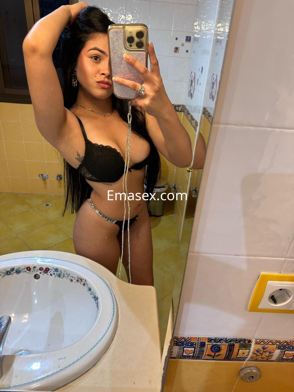 Puta en Málaga posando en un baño, lleva lencería negra y muestra su cabello largo y liso.
