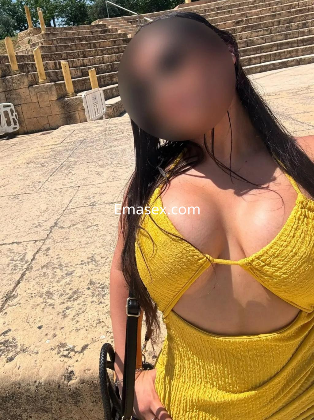 Puta en Coruña luce un vestido amarillo ajustado con escote pronunciado, posando en un entorno al aire libre.