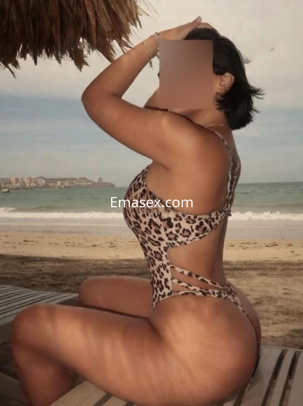 Escort en Alicante sentada en la playa, luciendo un bañador de estampado animal y destacando su figura.