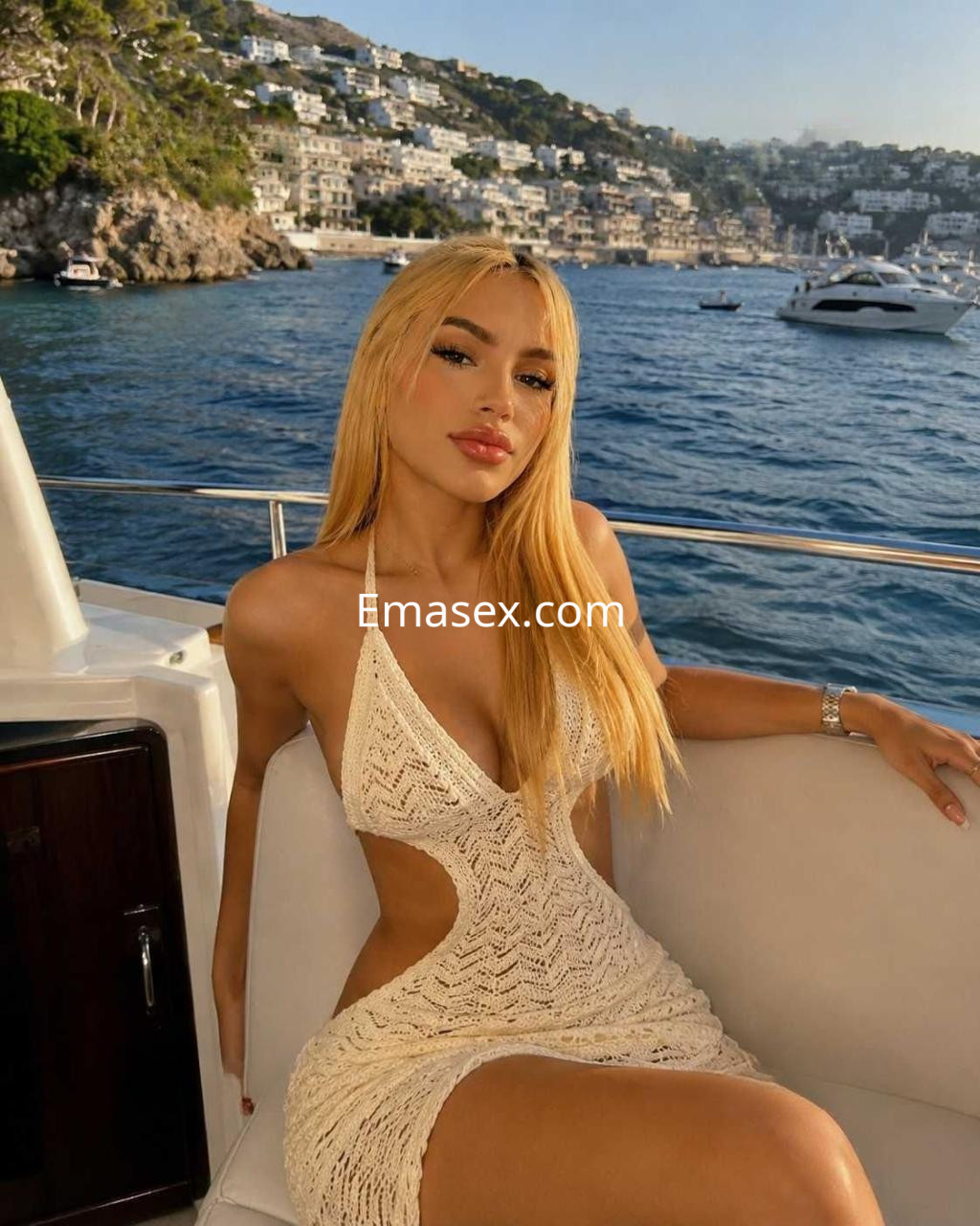 Escort en Alicante con cabello rubio, vestida con un vestido de crochet blanco, posando en un yate frente al mar.