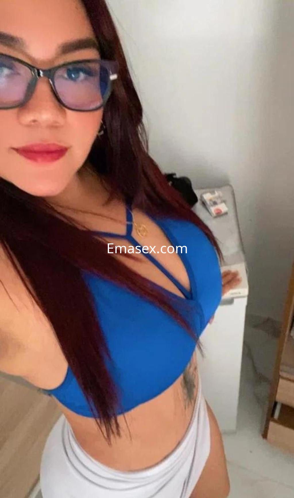 Escort en Alicante con cabello largo y rojizo, usando un top azul y una falda blanca, sonriendo a la cámara.
