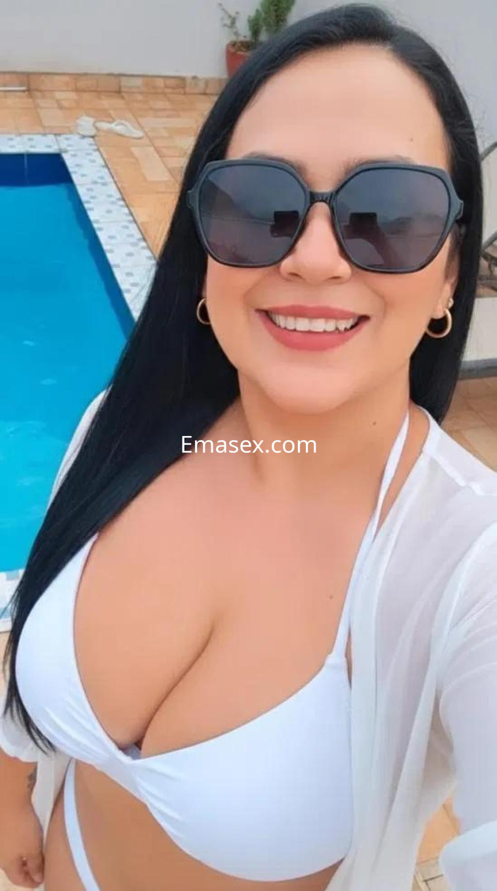 La puta posa sonriente junto a una piscina, luciendo un bikini blanco y gafas de sol, en Alicante.