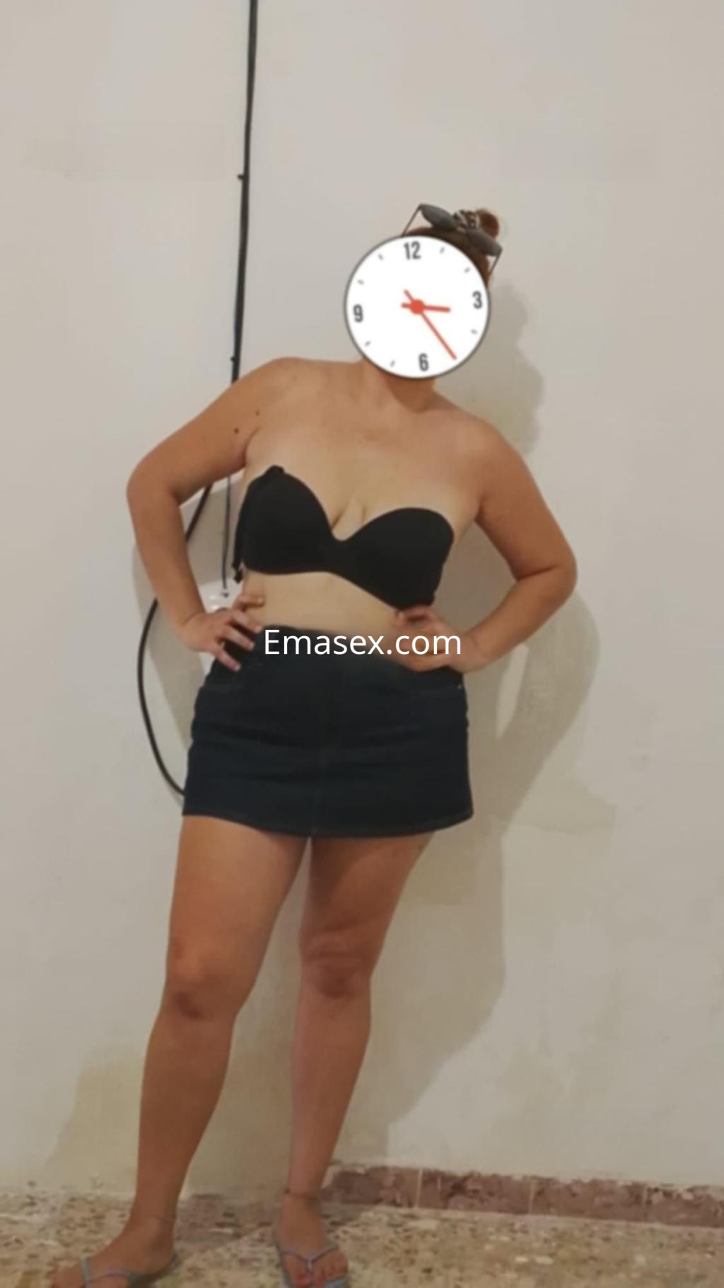 Puta en Almería viste un sujetador negro y una falda corta, posando con una mano en la cadera.
