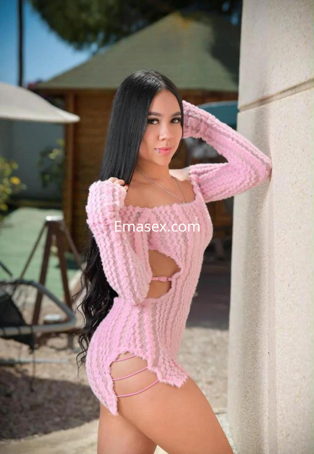 Puta en Almería con vestido de punto rosa, mostrando cortes laterales, posando con una mano en la cadera.