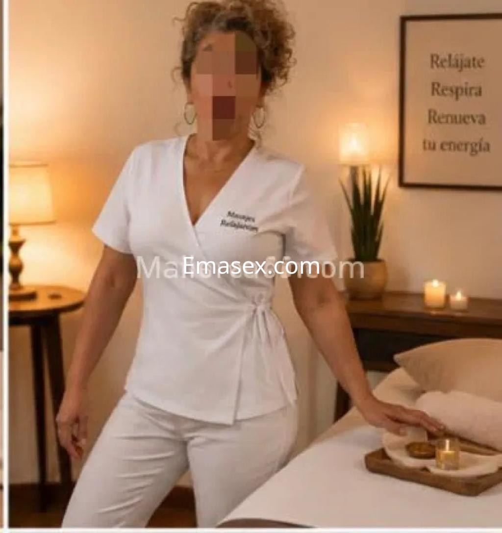 La puta en Palma de Mallorca viste una blusa blanca y pantalones claros, posando en un ambiente acogedor.