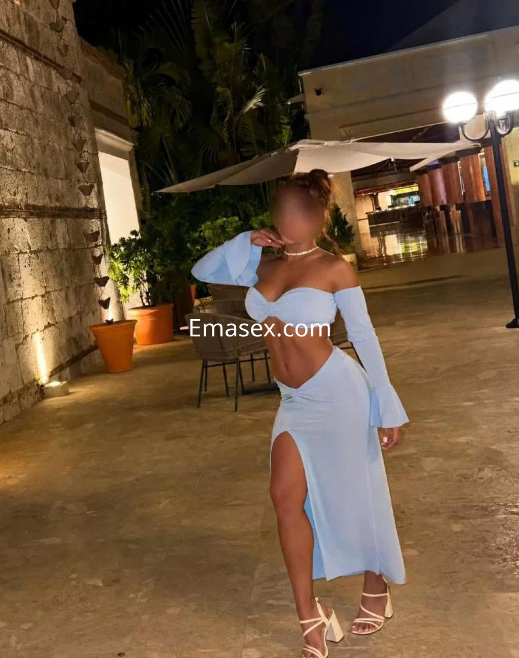 Escort en Palma de Mallorca con vestido azul claro, mangas acampanadas y una pose coqueta en un ambiente al aire libre.