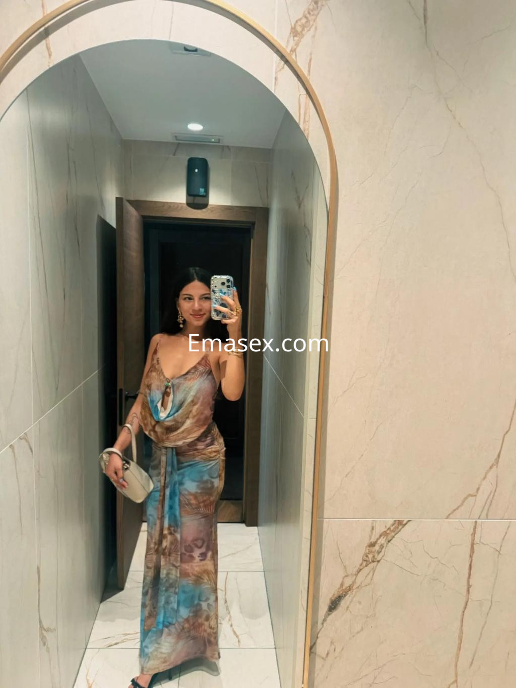 Escort en Palma de Mallorca luciendo un vestido largo y fluido, posando frente a un espejo en un entorno elegante.