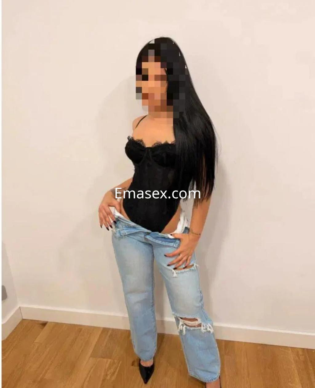 Puta en Burgos viste un body negro con tirantes y pantalones vaqueros desgastados, posando con confianza.