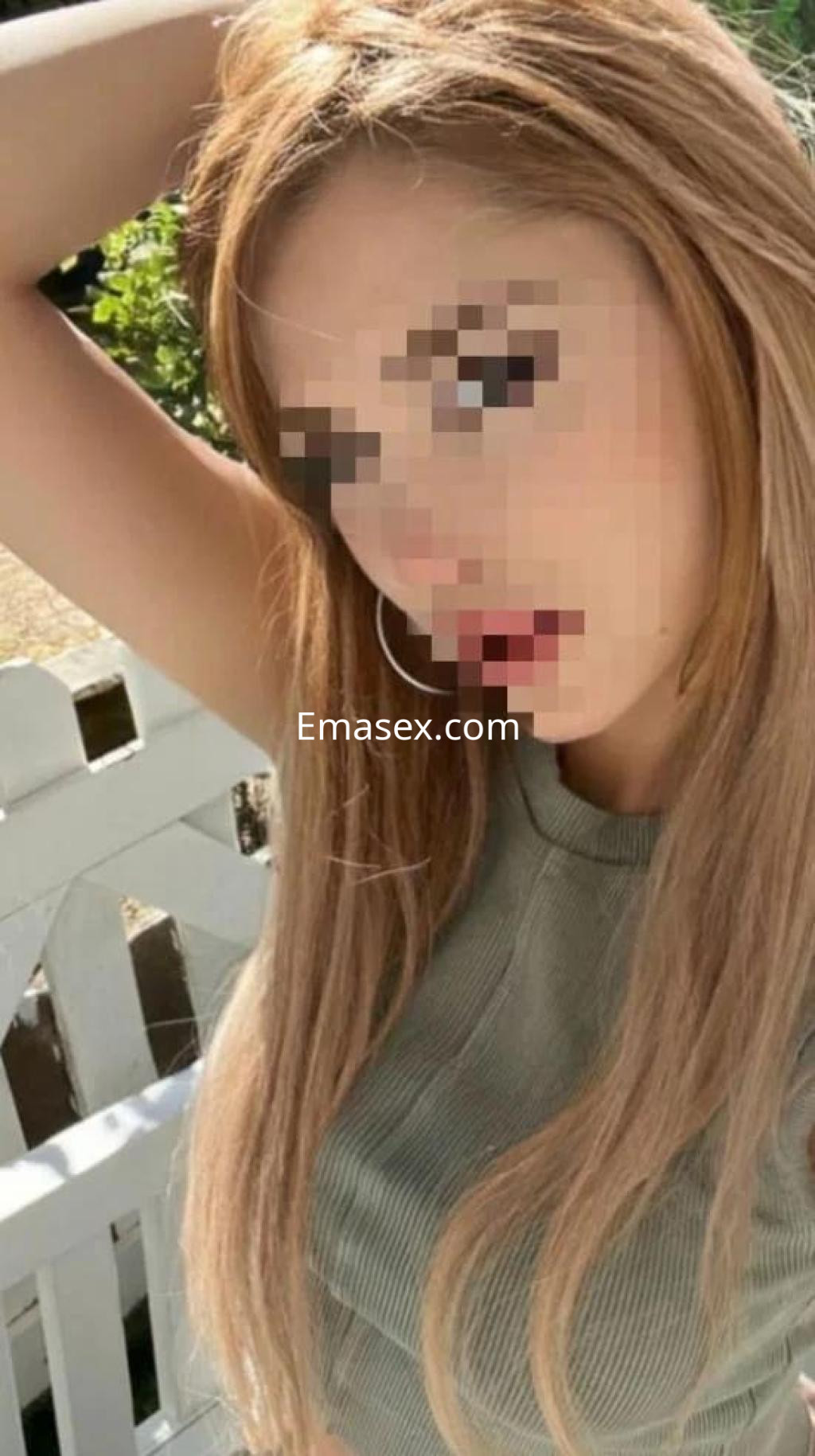 Puta con cabello largo y rubio, vestida con una blusa verde, posando de forma coqueta en Huelva.