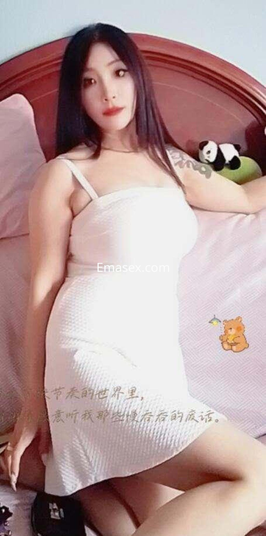 Escort en Madrid con cabello largo y negro, vistiendo un vestido blanco ajustado mientras posa en una cama.