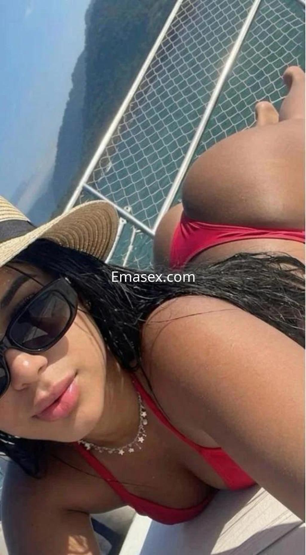 Puta en Madrid, luciendo un bikini rojo y sombrero, posando en un yate con el mar de fondo.