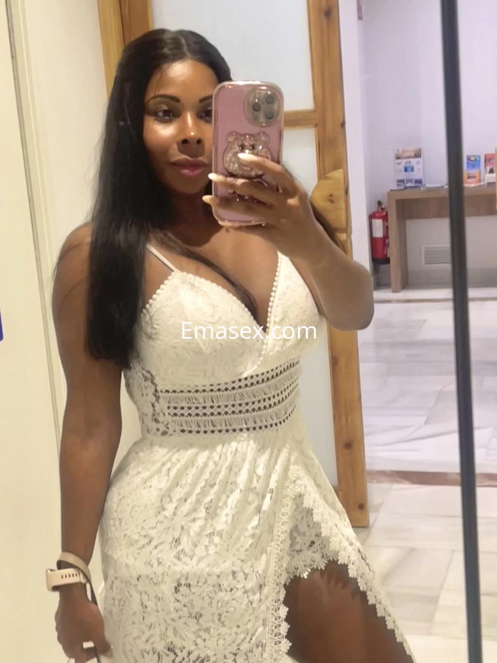 Escort en Málaga con vestido blanco de encaje, posando frente a un espejo, con cabello largo y lacio.
