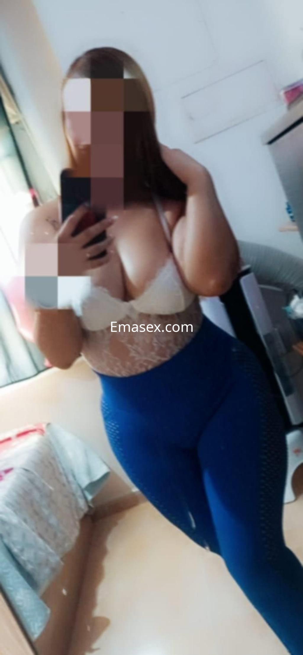 Escort en Valencia posando frente al espejo con un top blanco y leggings azules, mostrando una actitud coqueta.