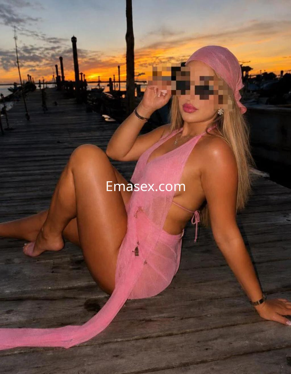 Puta posando en un muelle al atardecer, luciendo un vestido de malla rosa y un pañuelo en la cabeza en Valencia.