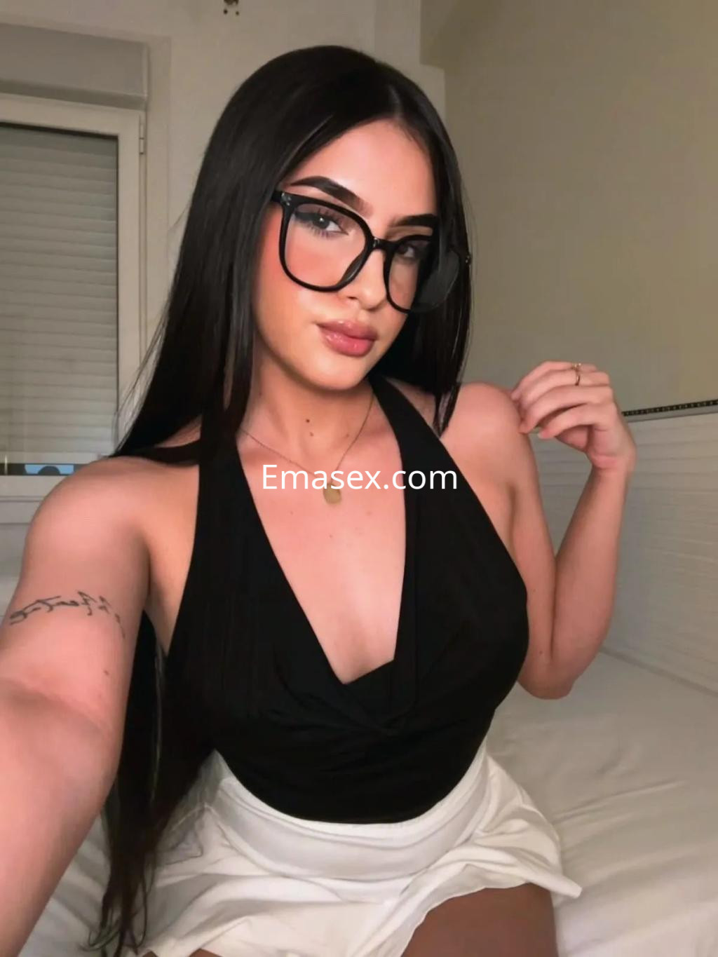 Escort en Bilbao con cabello largo y lacio, usando gafas, blusa negra y falda blanca, posando con confianza.