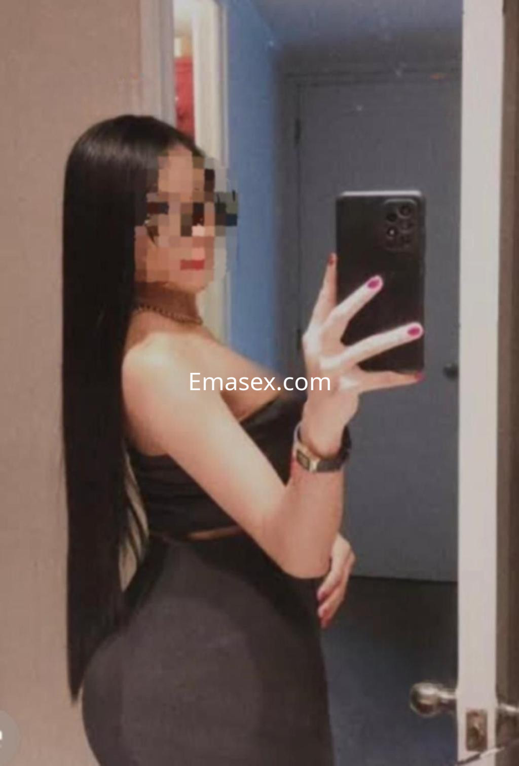 Escort en Albacete posando de perfil frente a un espejo, luciendo una blusa negra y con el cabello largo y liso.