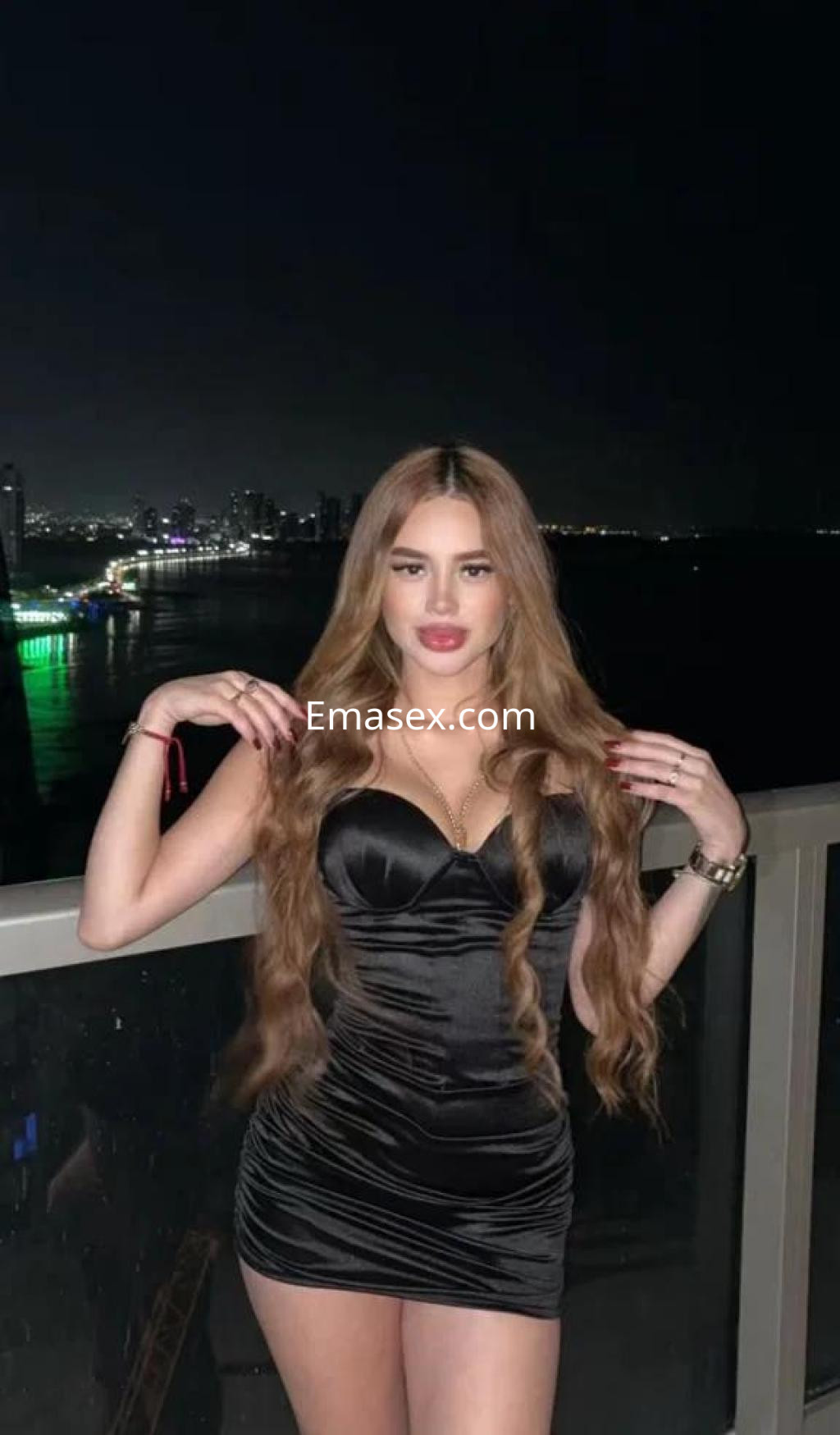 Puta posando en un balcón con vistas nocturnas, viste un vestido negro ajustado y tiene el cabello largo y suelto en Alicante.