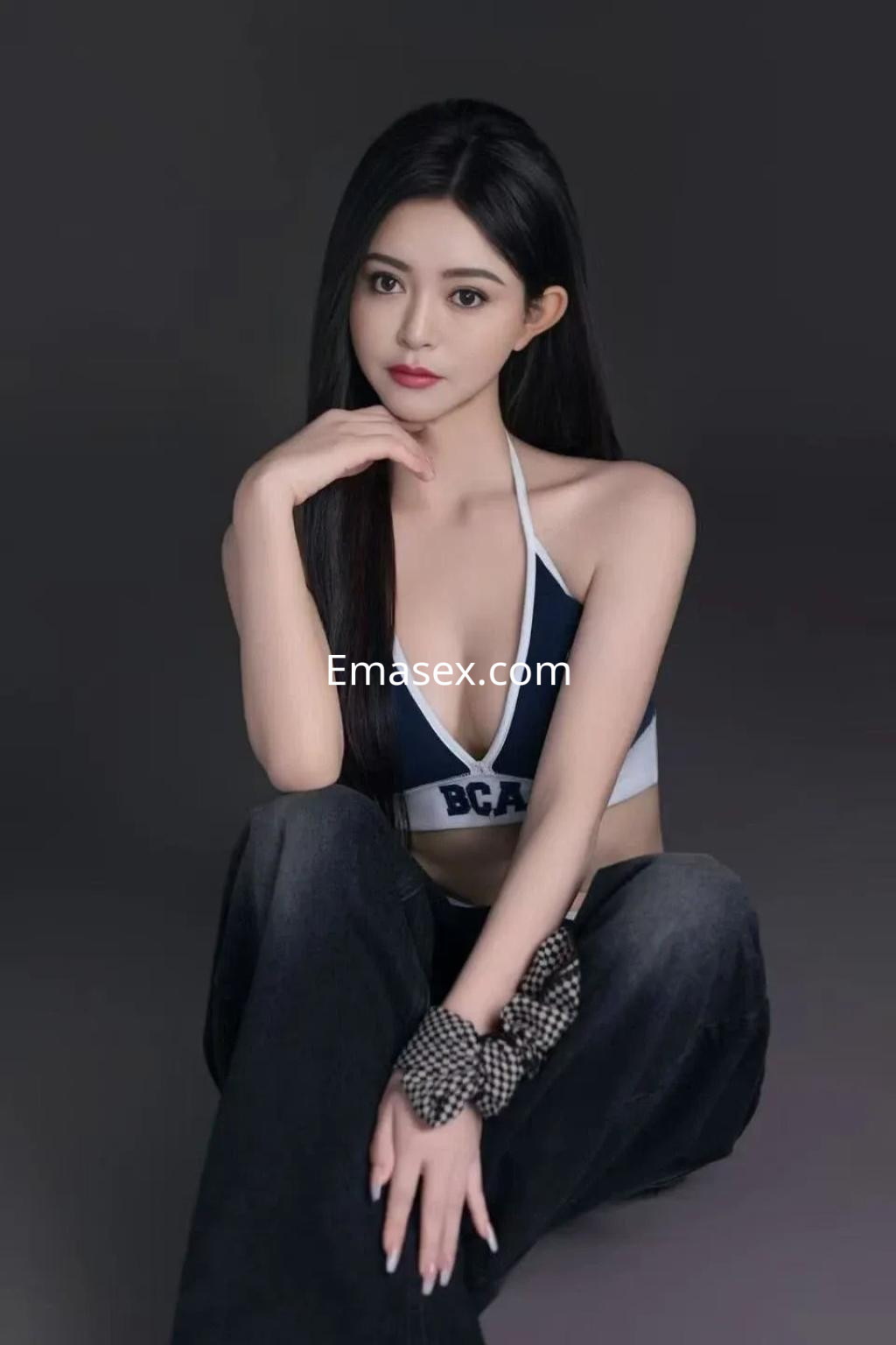 Escort en Alicante con cabello largo y oscuro, vestida con top deportivo y jeans, posando sentada.