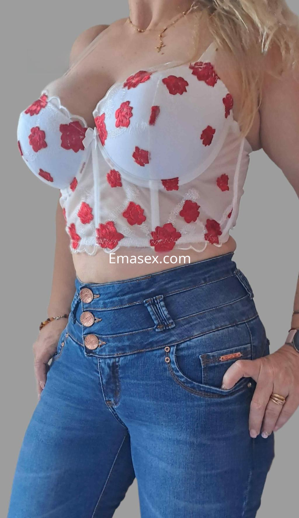 La puta viste un top blanco con flores rojas y jeans ajustados, mostrando una pose coqueta en Badajoz.