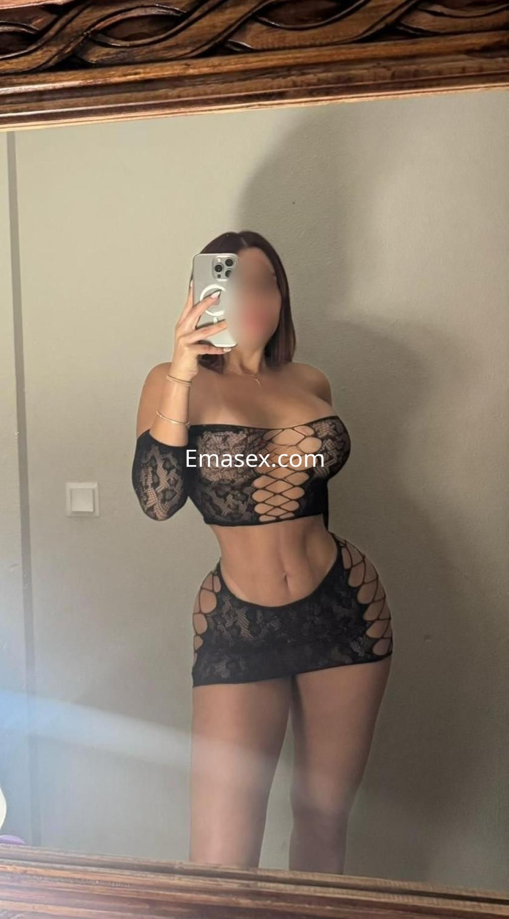 Escort en Ibiza, posando frente a un espejo con un vestido de encaje negro que resalta su figura.