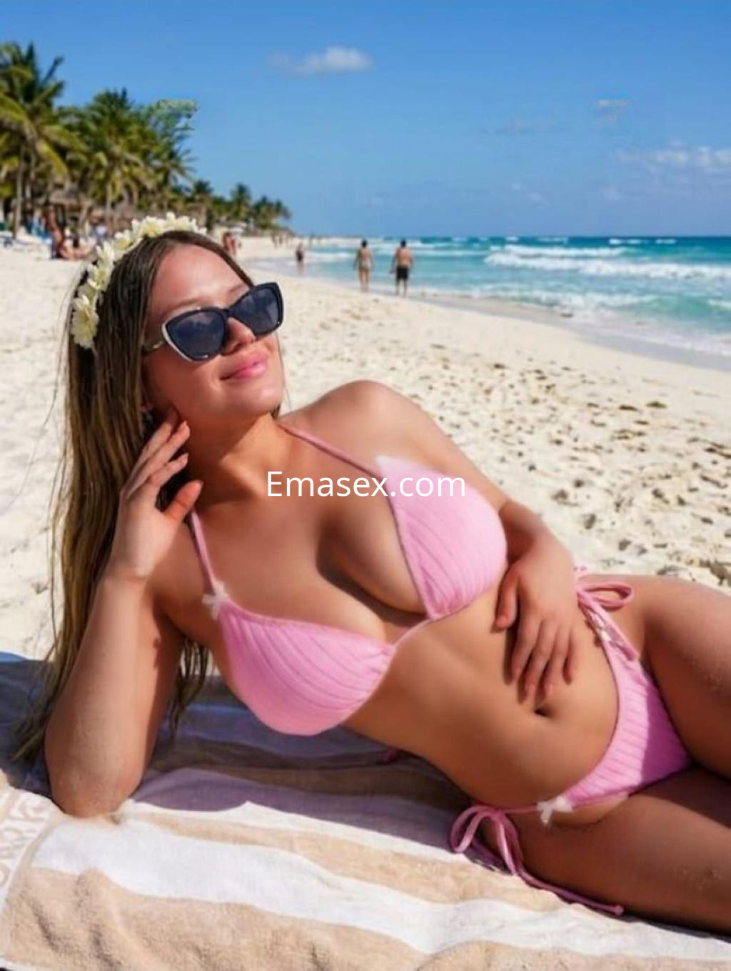 Escort en Ibiza descansando en la playa, lleva un bikini rosa, gafas de sol y flores en el cabello.