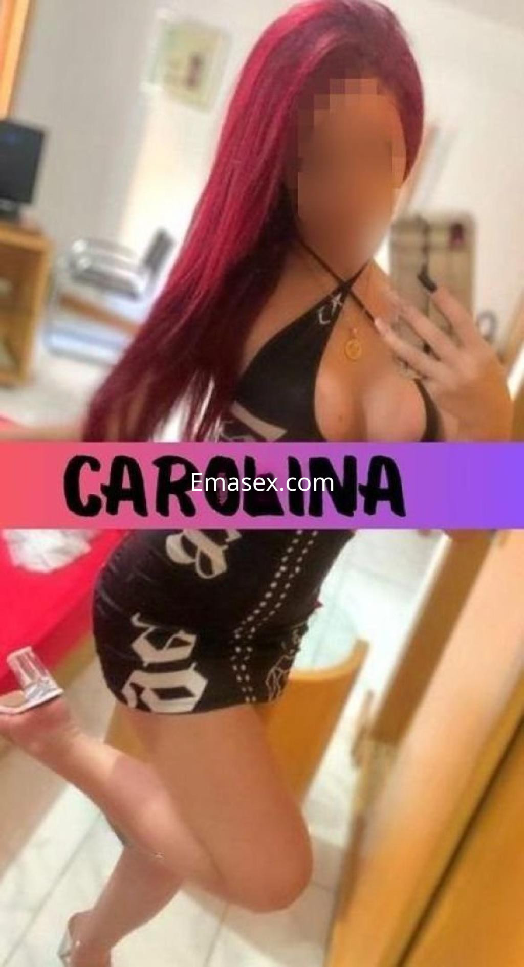 Escort en Cádiz posando con un vestido negro ajustado y sandalias transparentes, mostrando su cabello largo y rojizo.