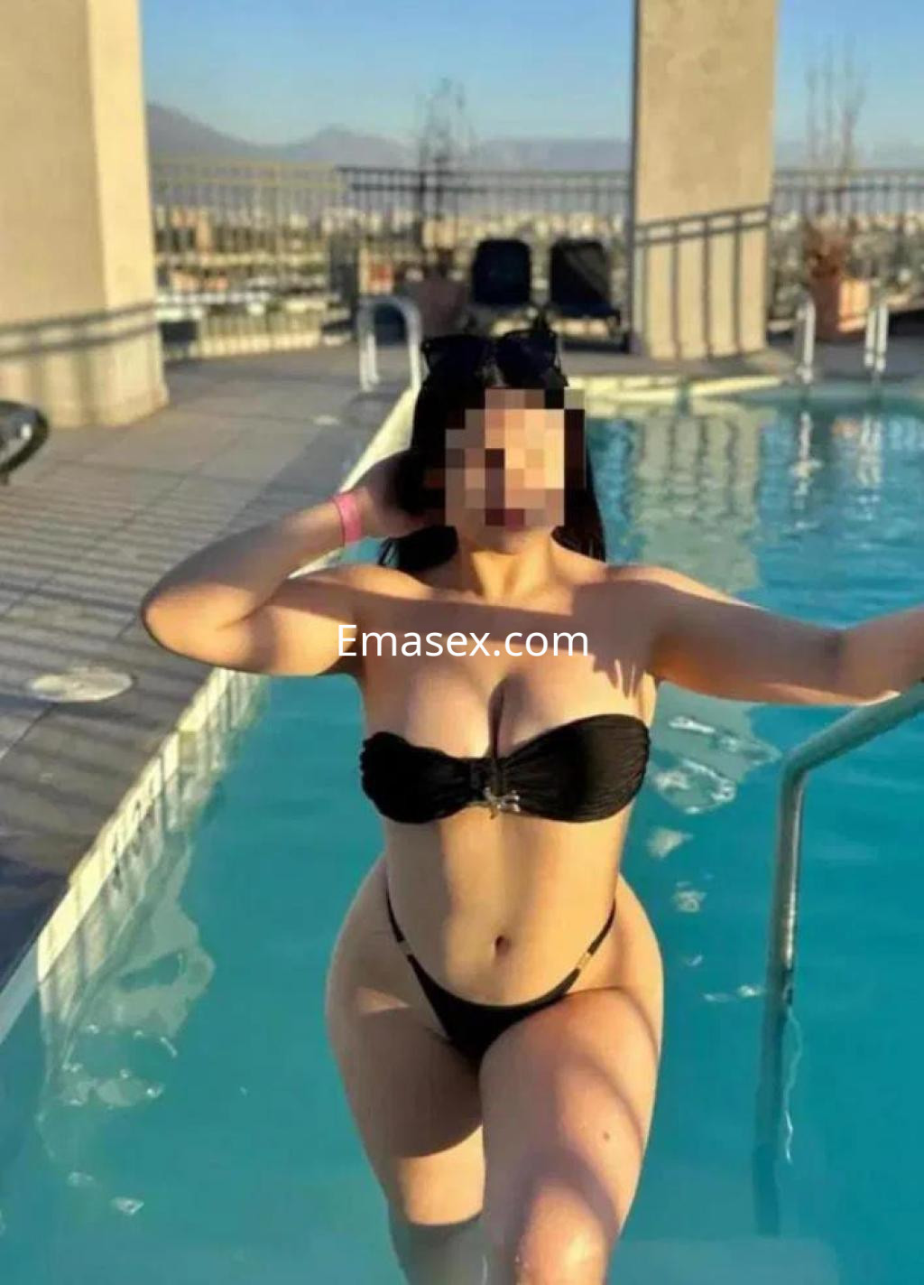 Escort en Huelva posando junto a una piscina, luciendo un bikini negro y mostrando una pose relajada.