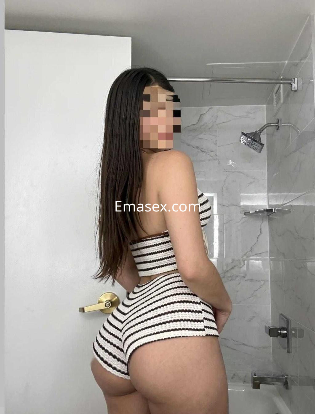 Puta posando de espaldas en un baño, viste un conjunto de rayas blanco y negro, con el cabello largo y lacio en Madrid.