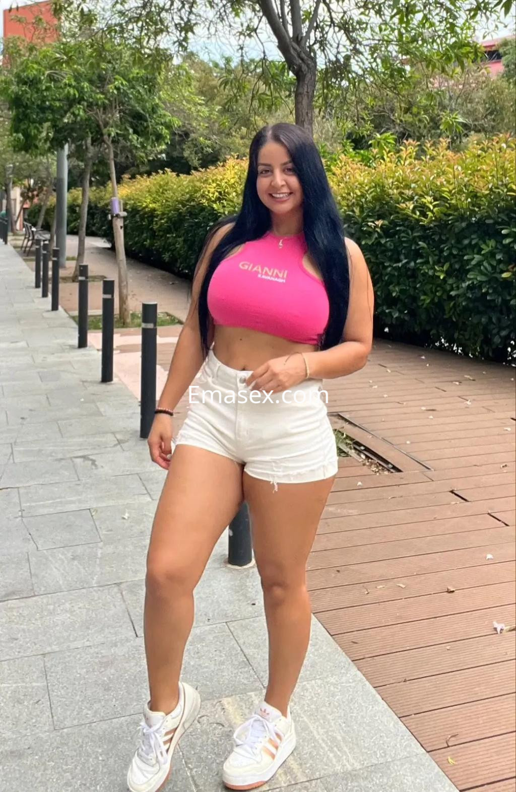 Puta con cabello largo y oscuro, vistiendo top rosa y shorts blancos, posando en una calle de Sevilla.