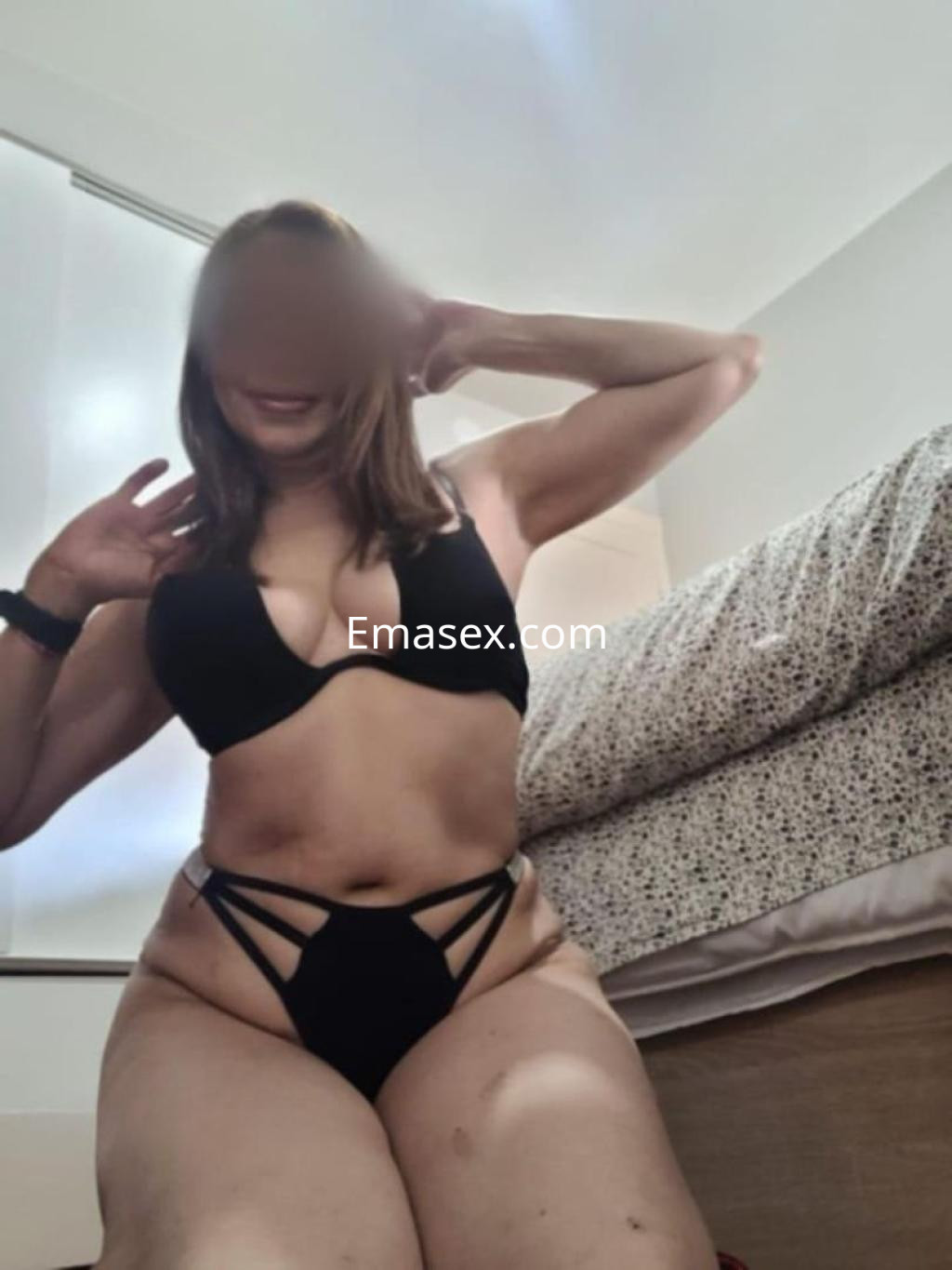 Escort en Toledo, posando con un sujetador negro y una lencería que destaca su figura, en un ambiente doméstico.