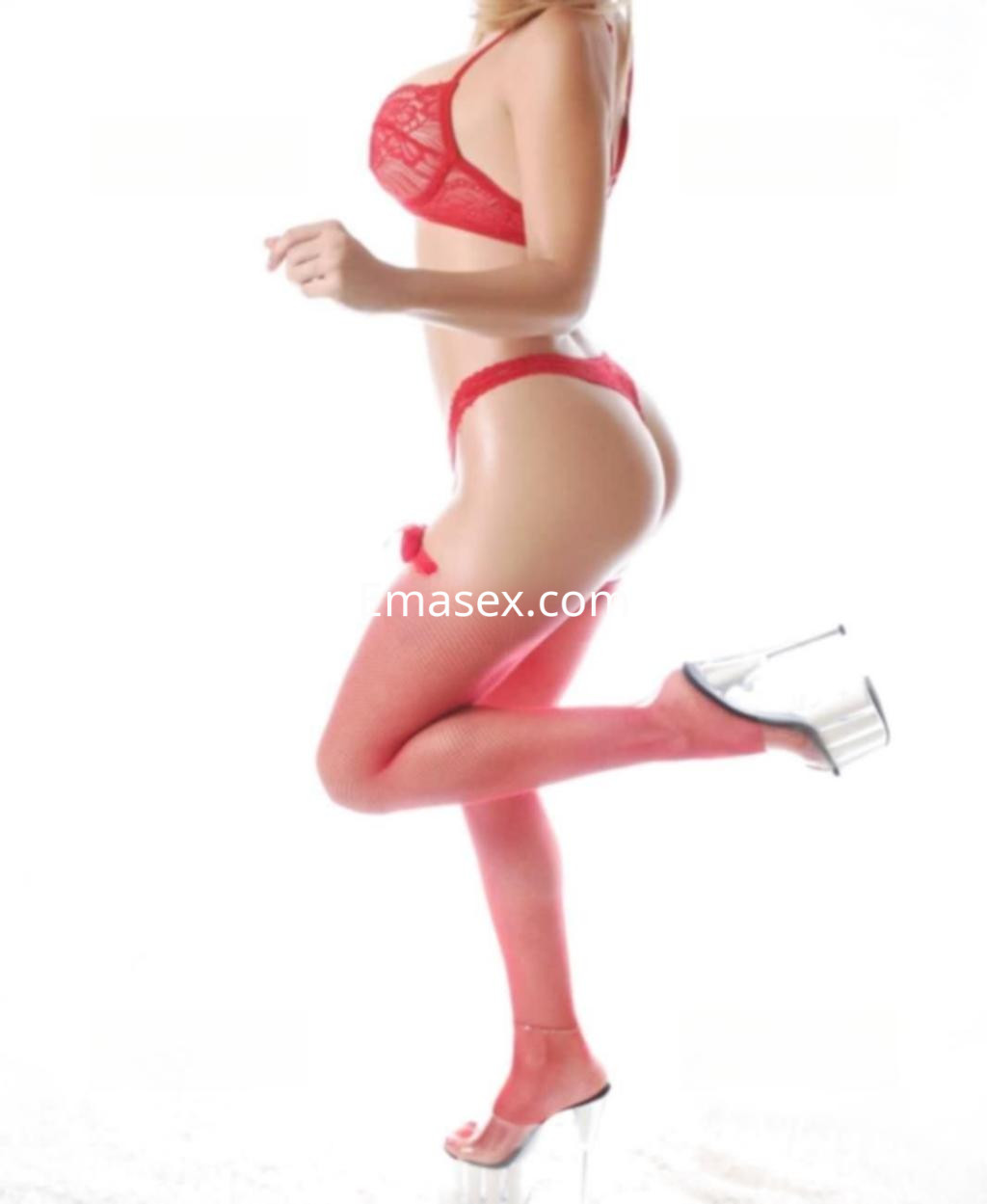 Escort en Toledo posando de perfil con lencería roja y medias, complementadas con tacones altos.