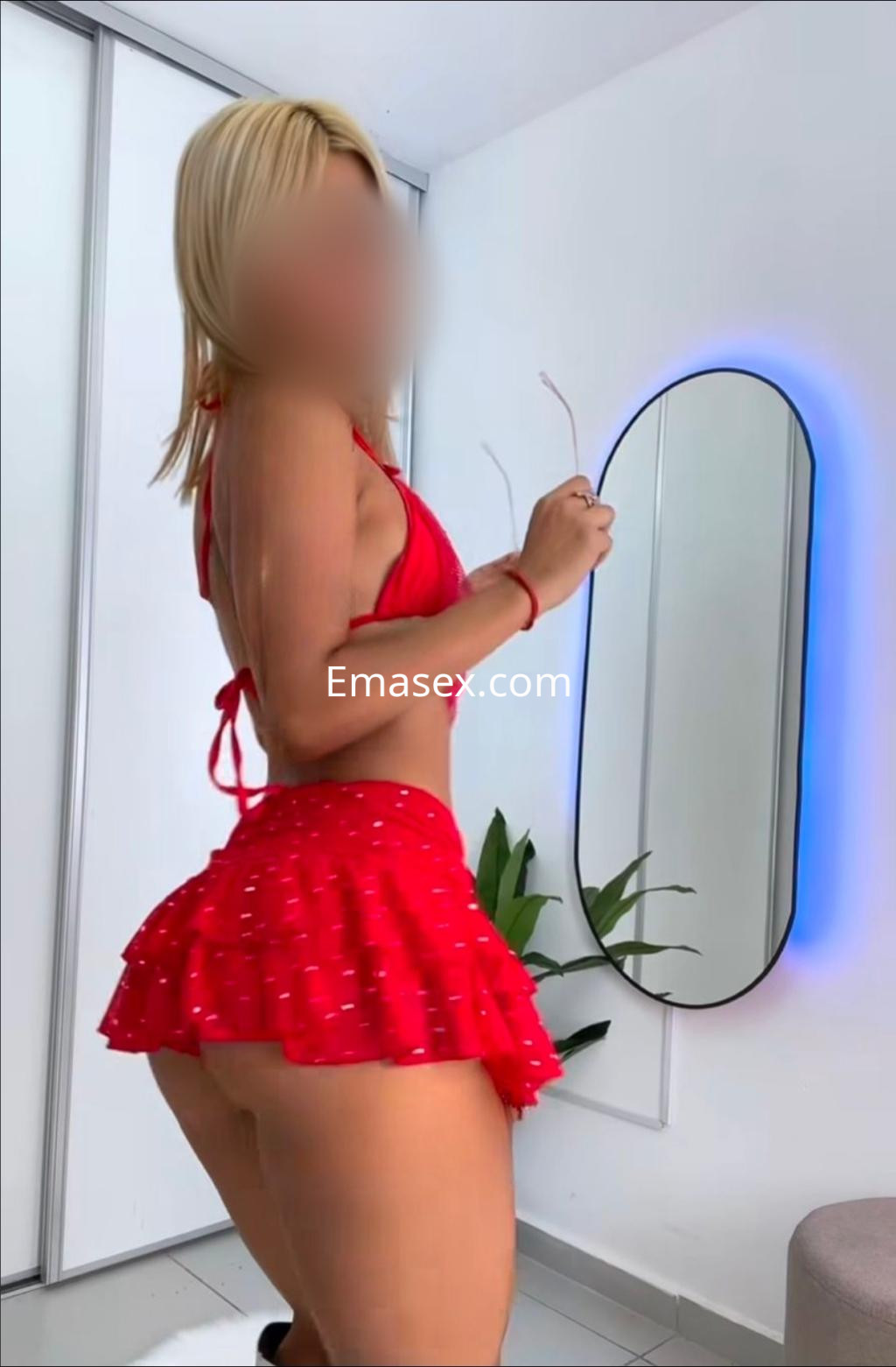 Puta en Tenerife luce un vestido corto rojo con detalles blancos, posando frente a un espejo.