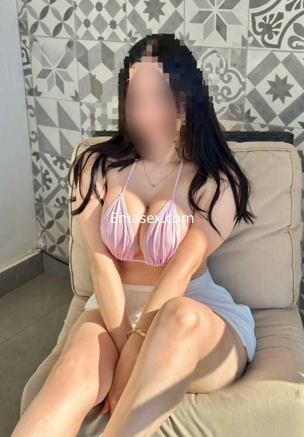 La puta posa sentada en un sofá, luciendo un top rosa claro y una falda blanca en un ambiente de Ibiza.