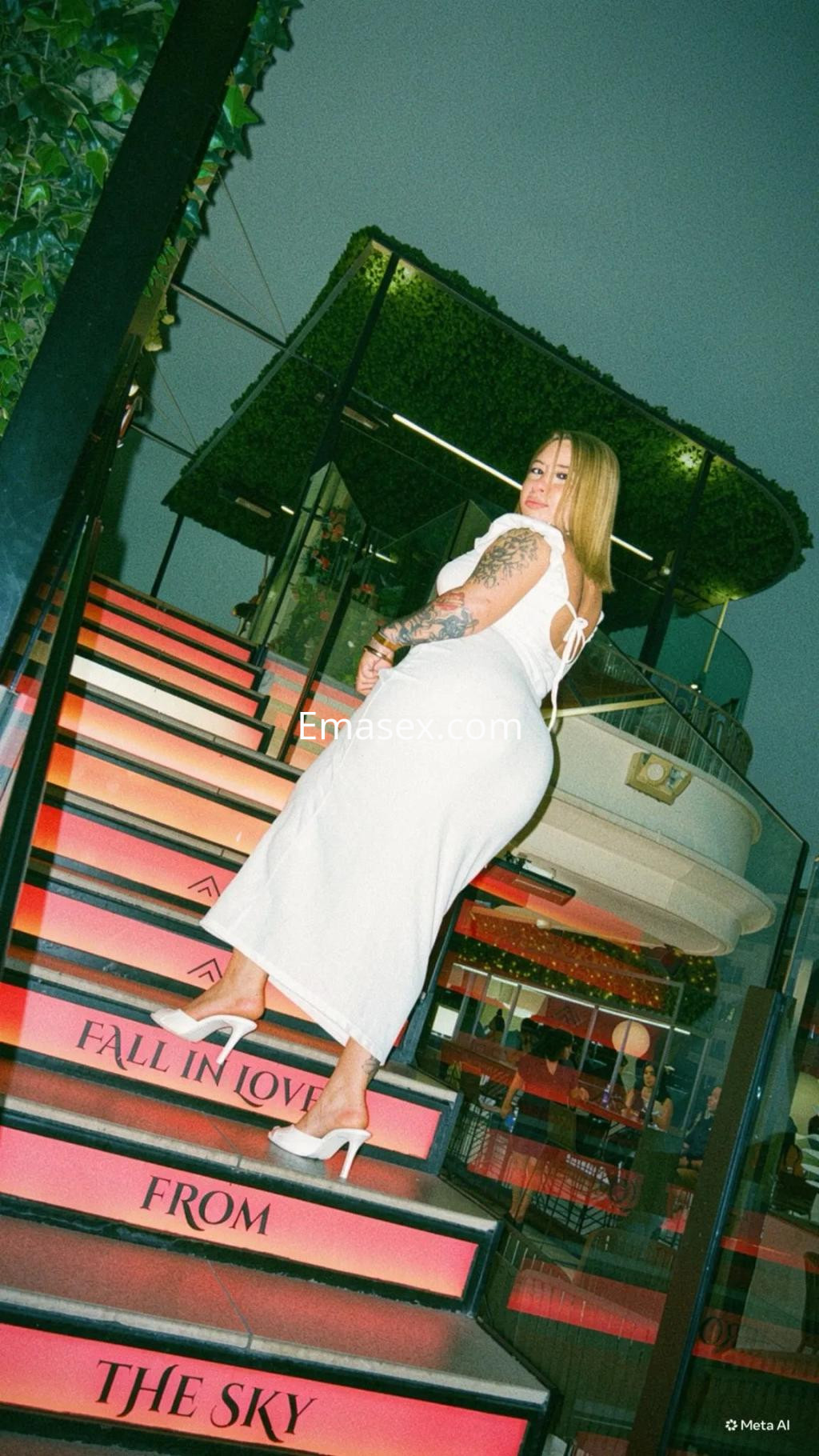 Puta con vestido blanco ajustado y tacones altos, posando en una escalera iluminada en Palma de Mallorca.