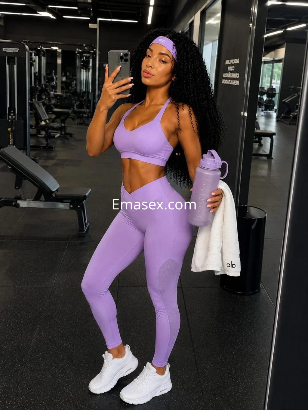Escort en Palma de Mallorca, posando en un gimnasio con un conjunto deportivo morado, cabello rizado y botella de agua.