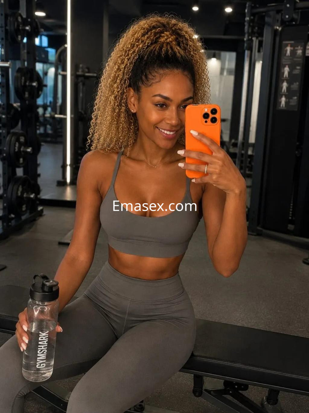 Escort en Palma de Mallorca posando en un gimnasio con ropa deportiva gris y sosteniendo una botella de agua.