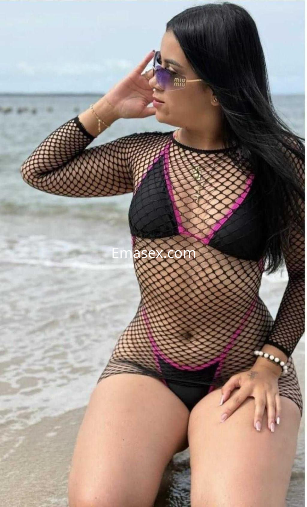 Puta sentada en la playa de Barcelona, luciendo una malla de red negra sobre un bikini negro con detalles rosas.