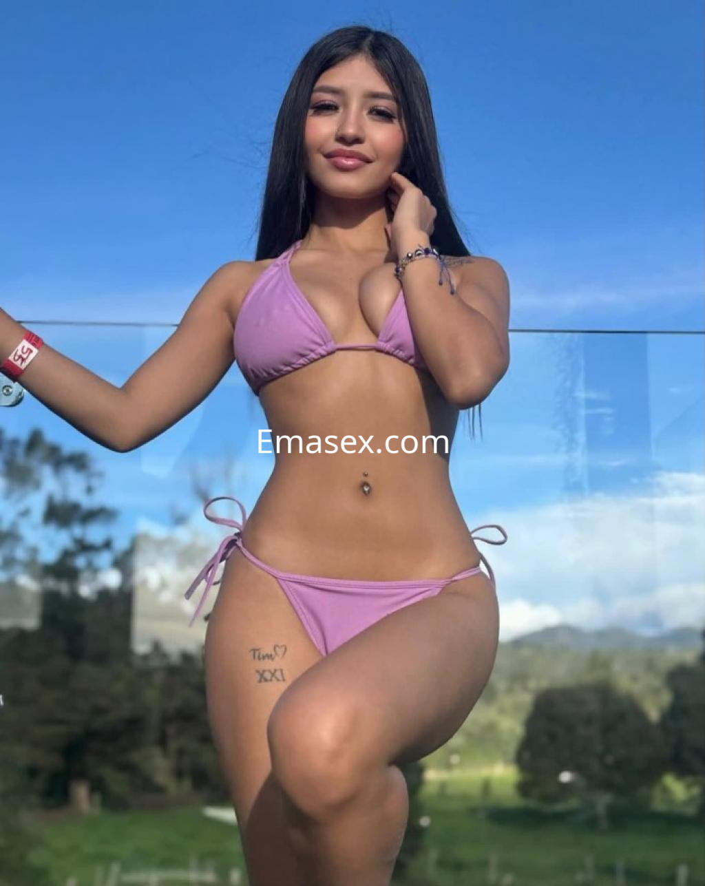 Escort en Castellón, luciendo un bikini rosa y posando de pie con un fondo natural despejado.