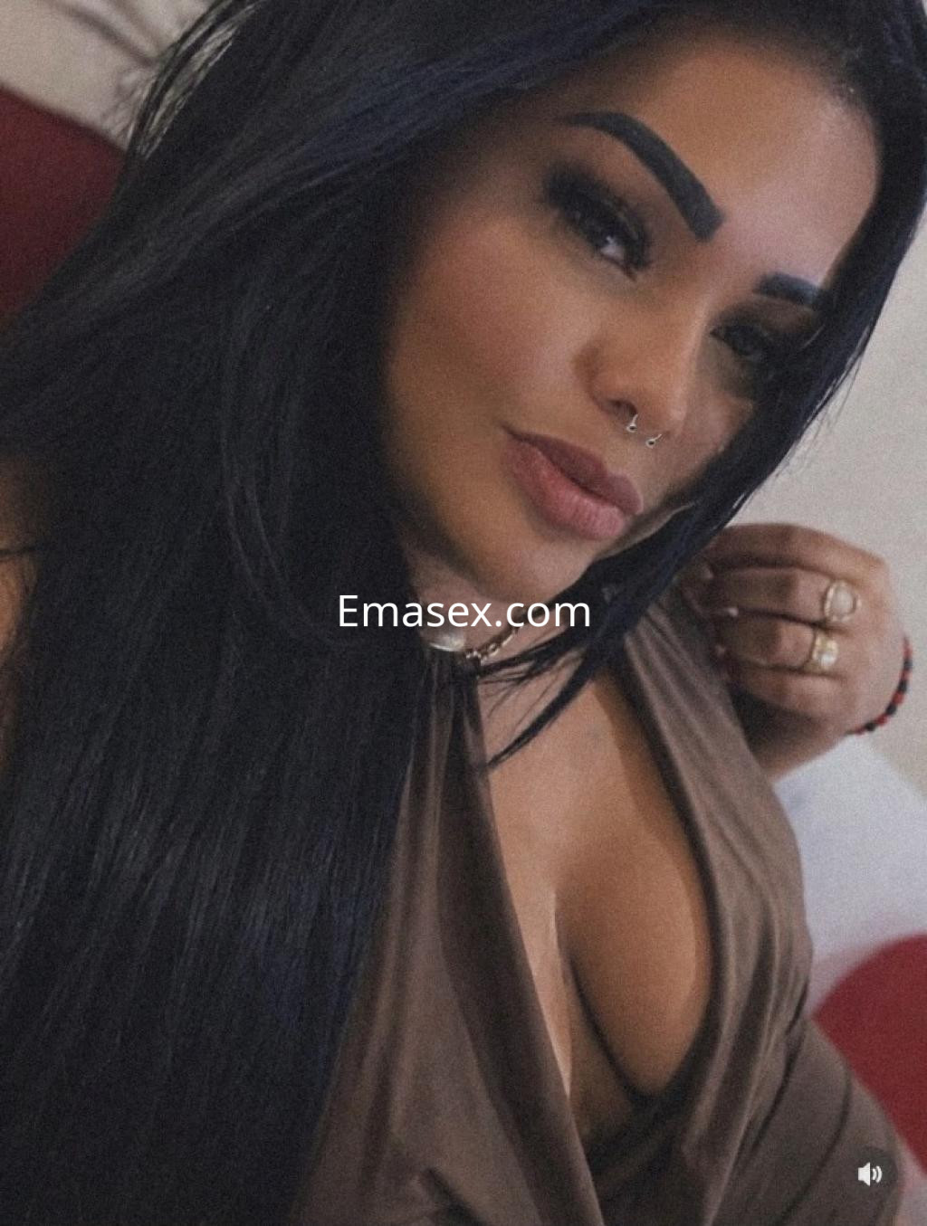 La escort en Lugo presenta un look atractivo con cabello largo y oscuro, luciendo una blusa marrón ajustada.