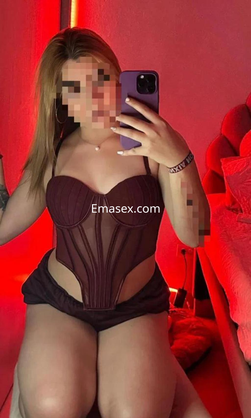 Escort en Madrid posando con un corset burdeos y shorts oscuros en un ambiente iluminado con luces rojas.