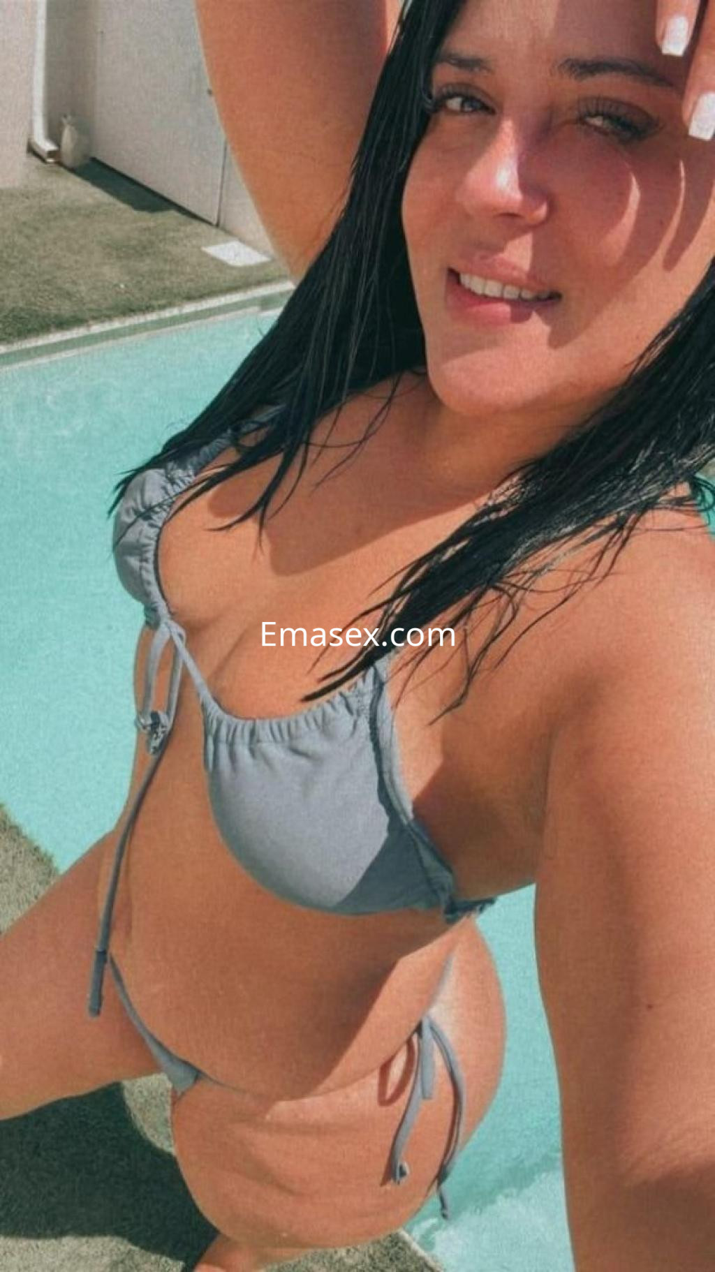 Escort en Málaga con cabello oscuro y lacio, posando junto a una piscina con bikini gris.