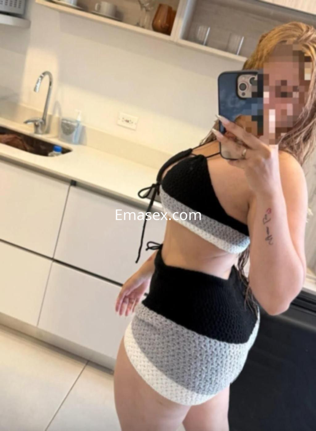 Puta en Pontevedra posando en un espejo, lleva un conjunto de bikini negro y gris, con cabello largo y ondulado.