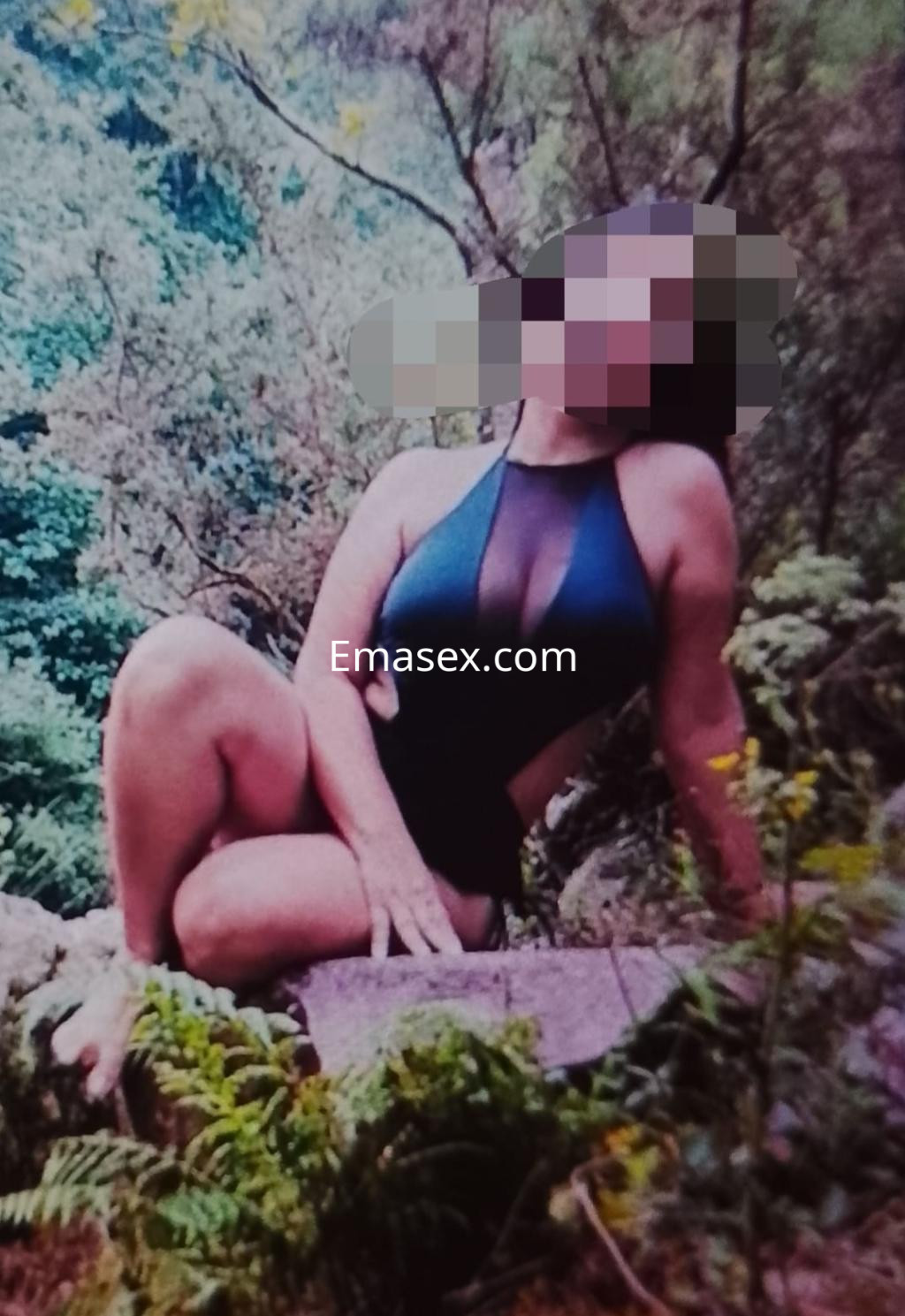 Escort en Donosti, sentada sobre una roca en un entorno natural, luciendo un traje de baño oscuro con transparencias.