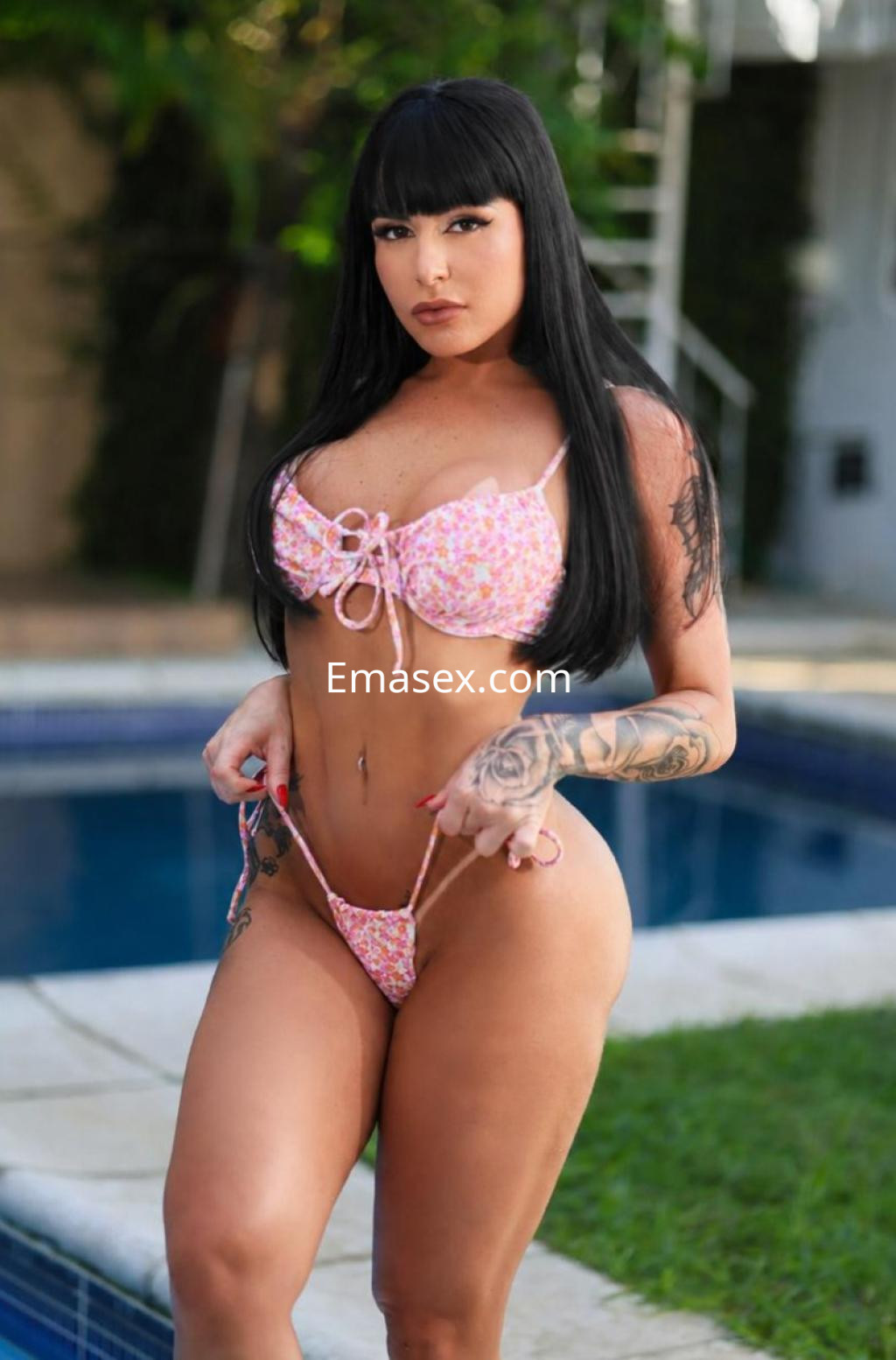 Puta en Bilbao con cabello negro y lacio, vistiendo un bikini rosa con estampado floral, posando junto a una piscina.