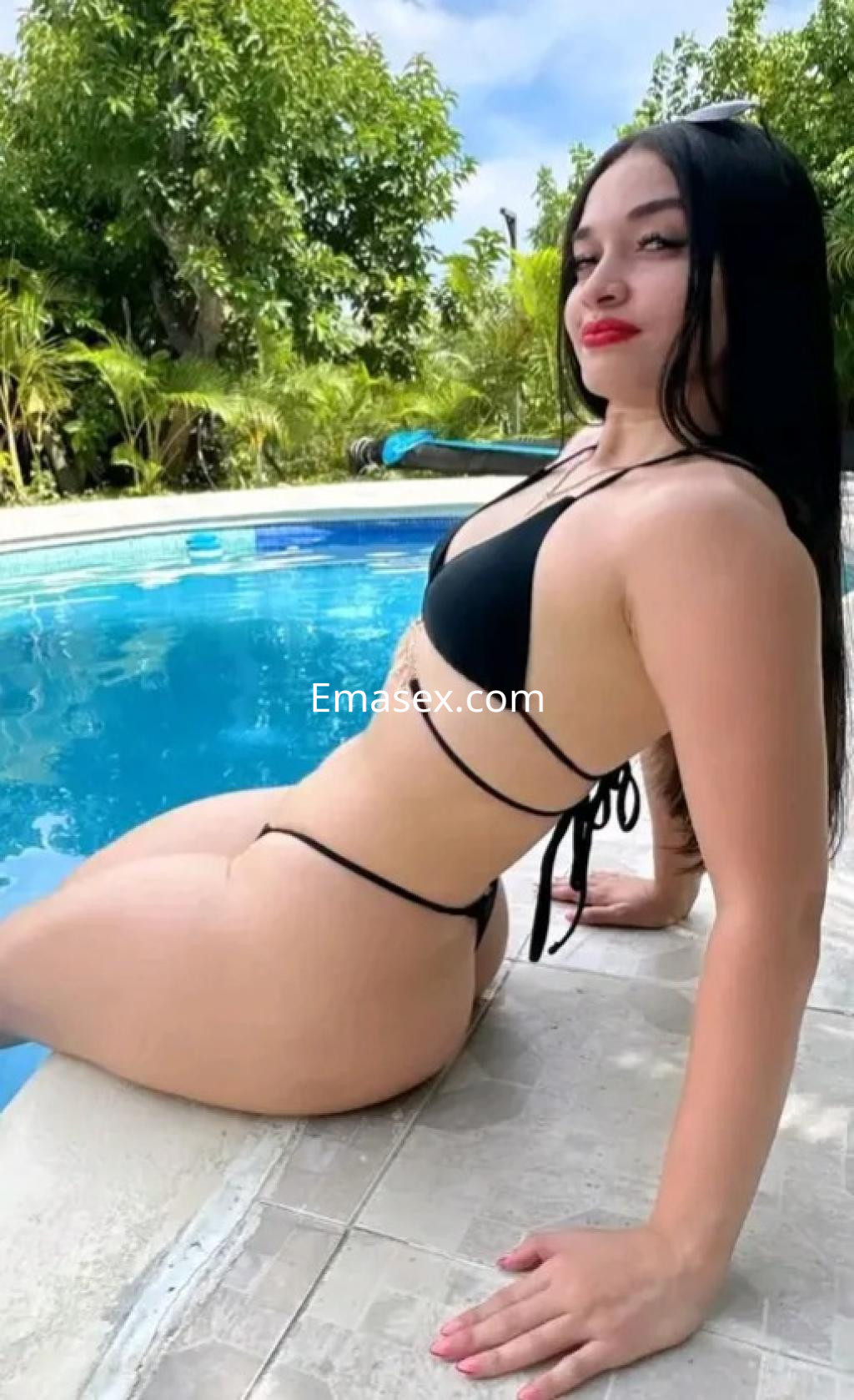 Escort en Bilbao, con cabello largo y lacio, viste un bikini negro y se relaja junto a una piscina.